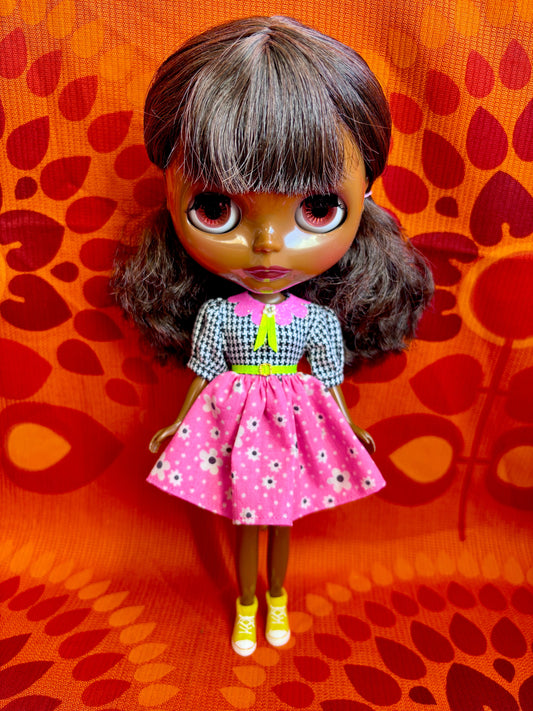 Doll wearing a pink dress with a floral pattern on an orange background with red floral designs.