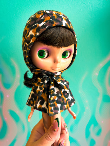 Doll with leopard print headscarf held against a teal background