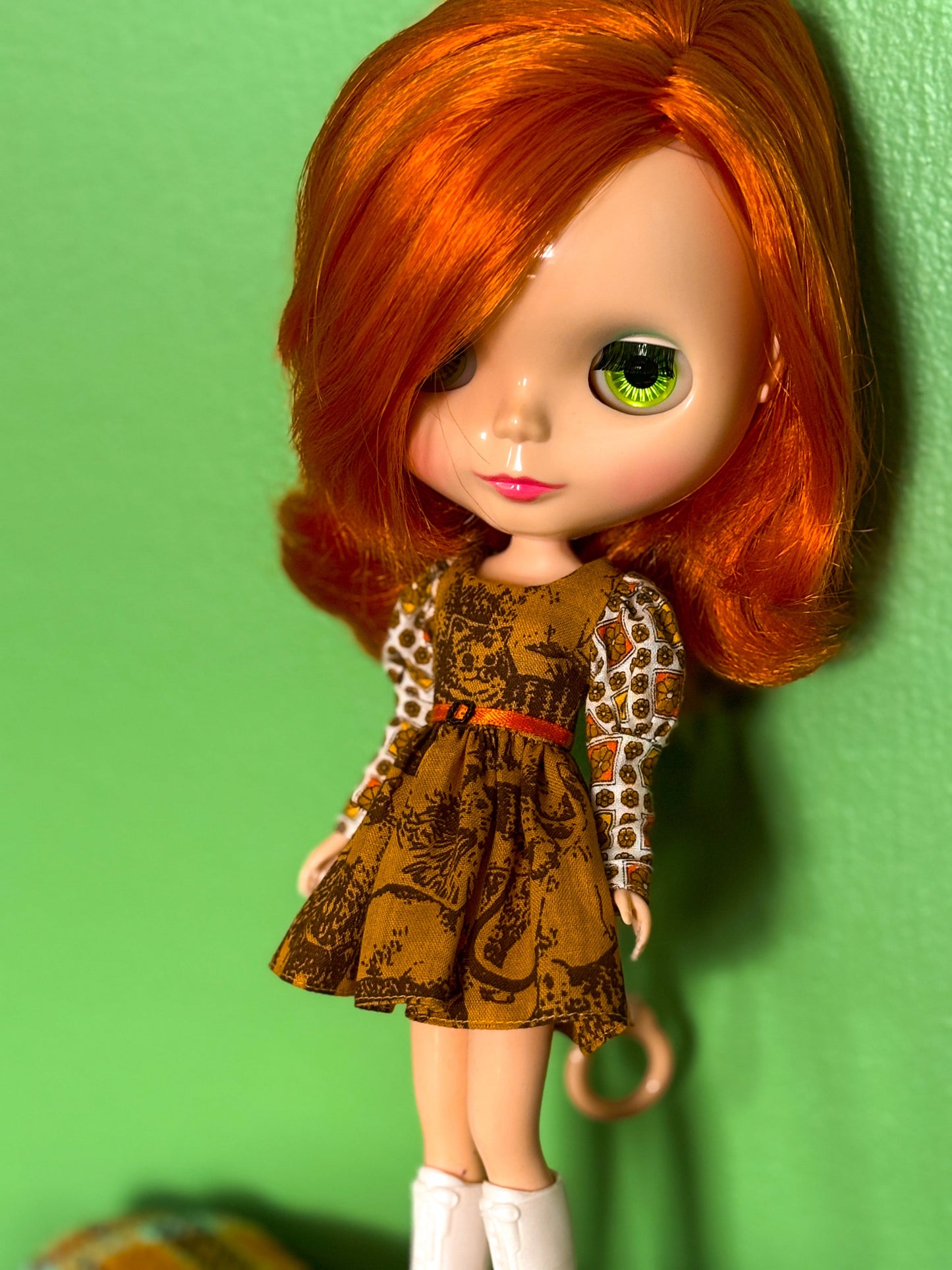 Doll with red hair and a patterned dress against a green background