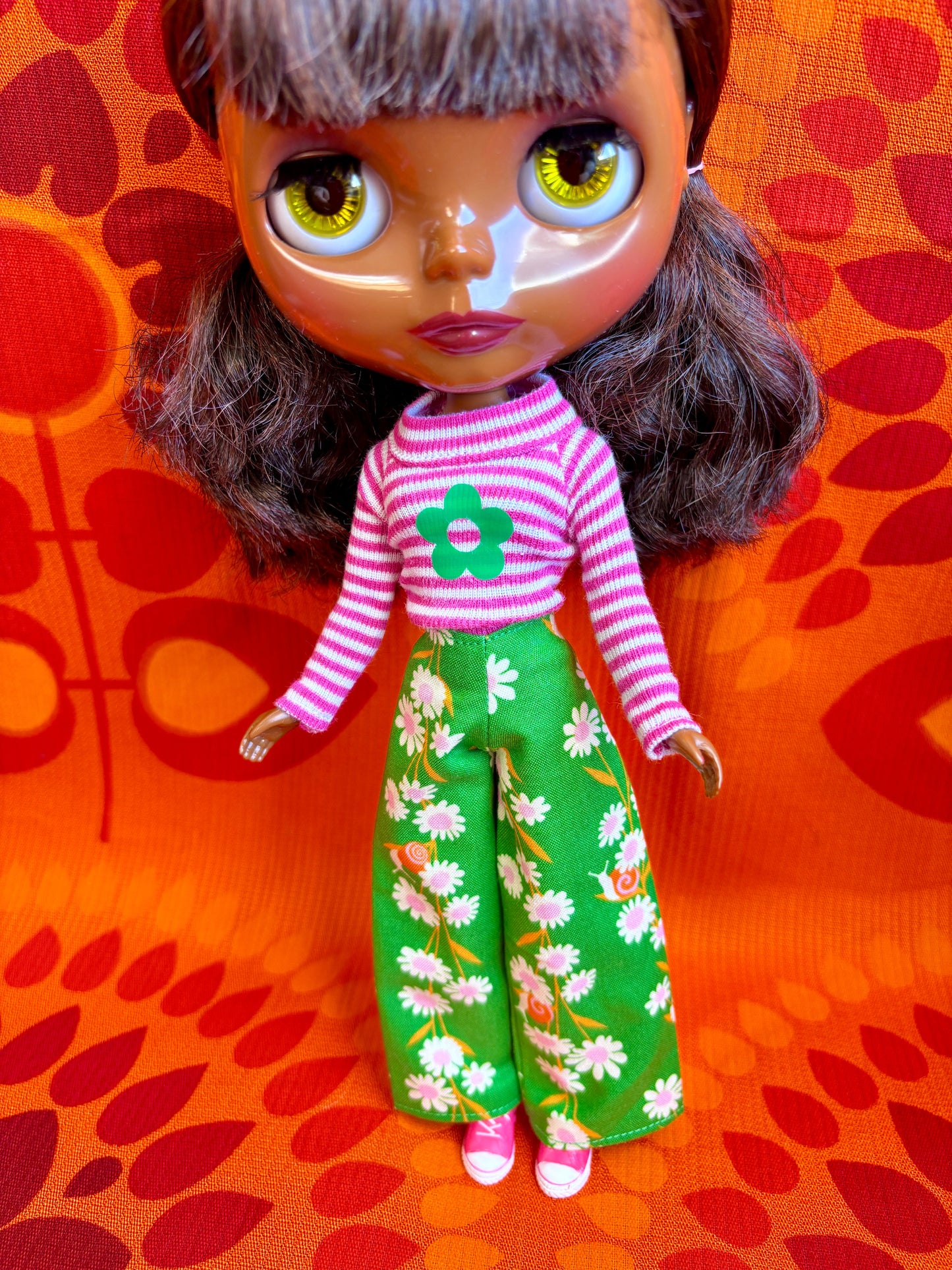 Doll with a pink and white striped shirt and green floral pants on an orange background