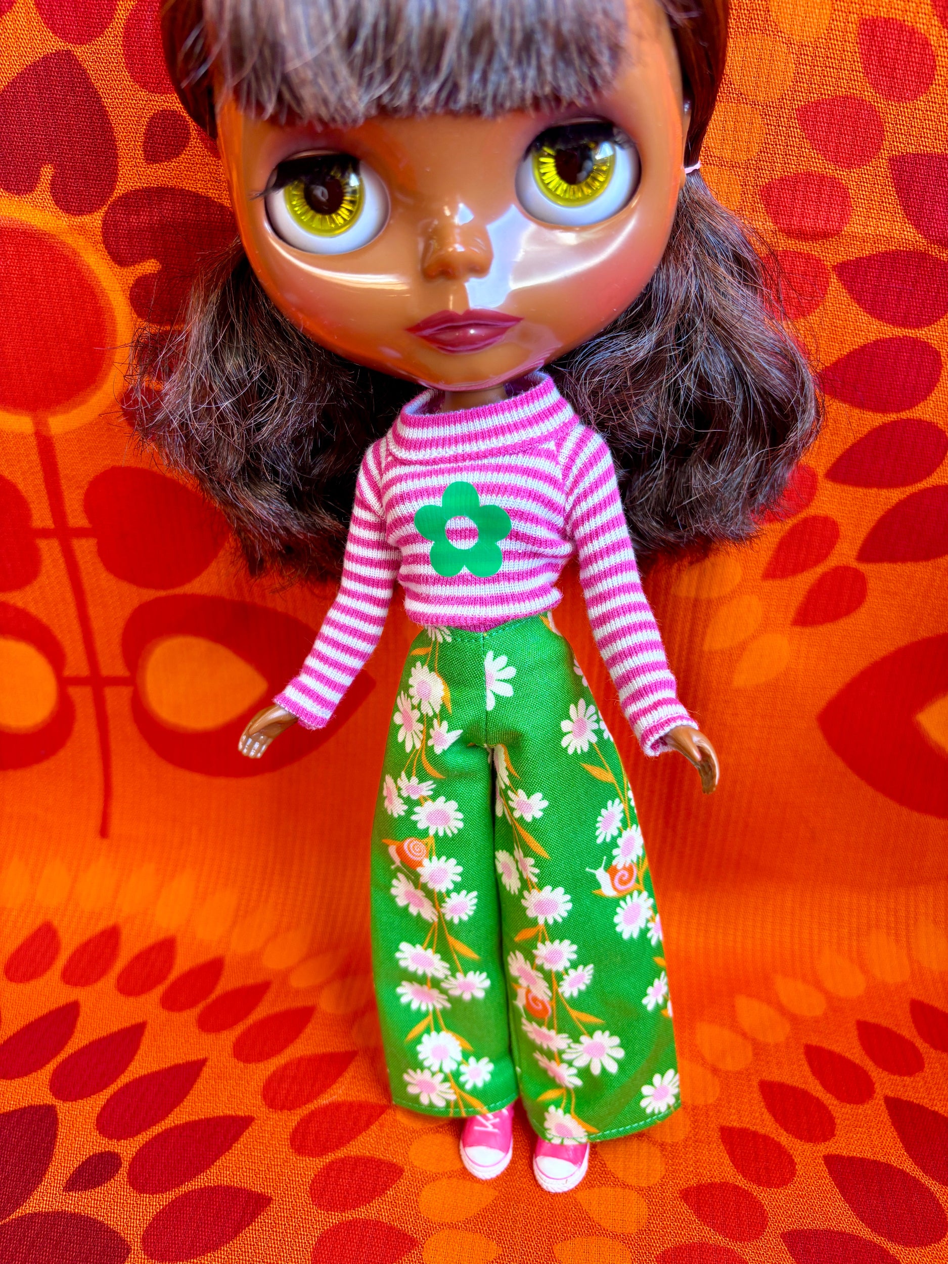 Doll with a pink and white striped shirt and green floral pants on an orange background