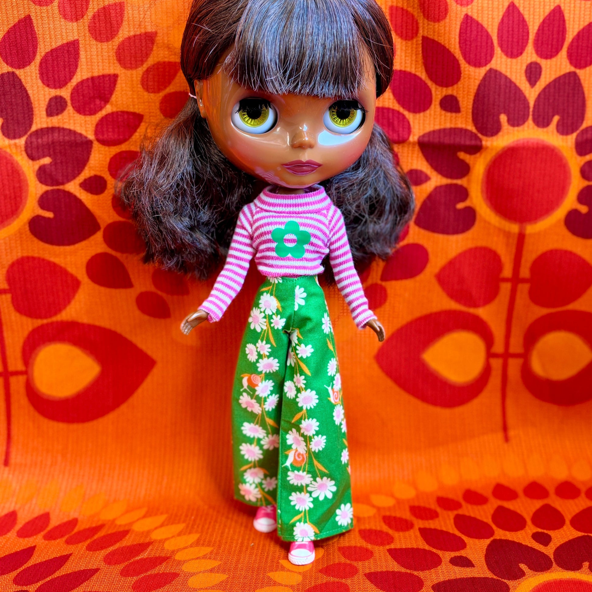 Doll wearing a pink striped shirt with a green flower and green floral pants on an orange background