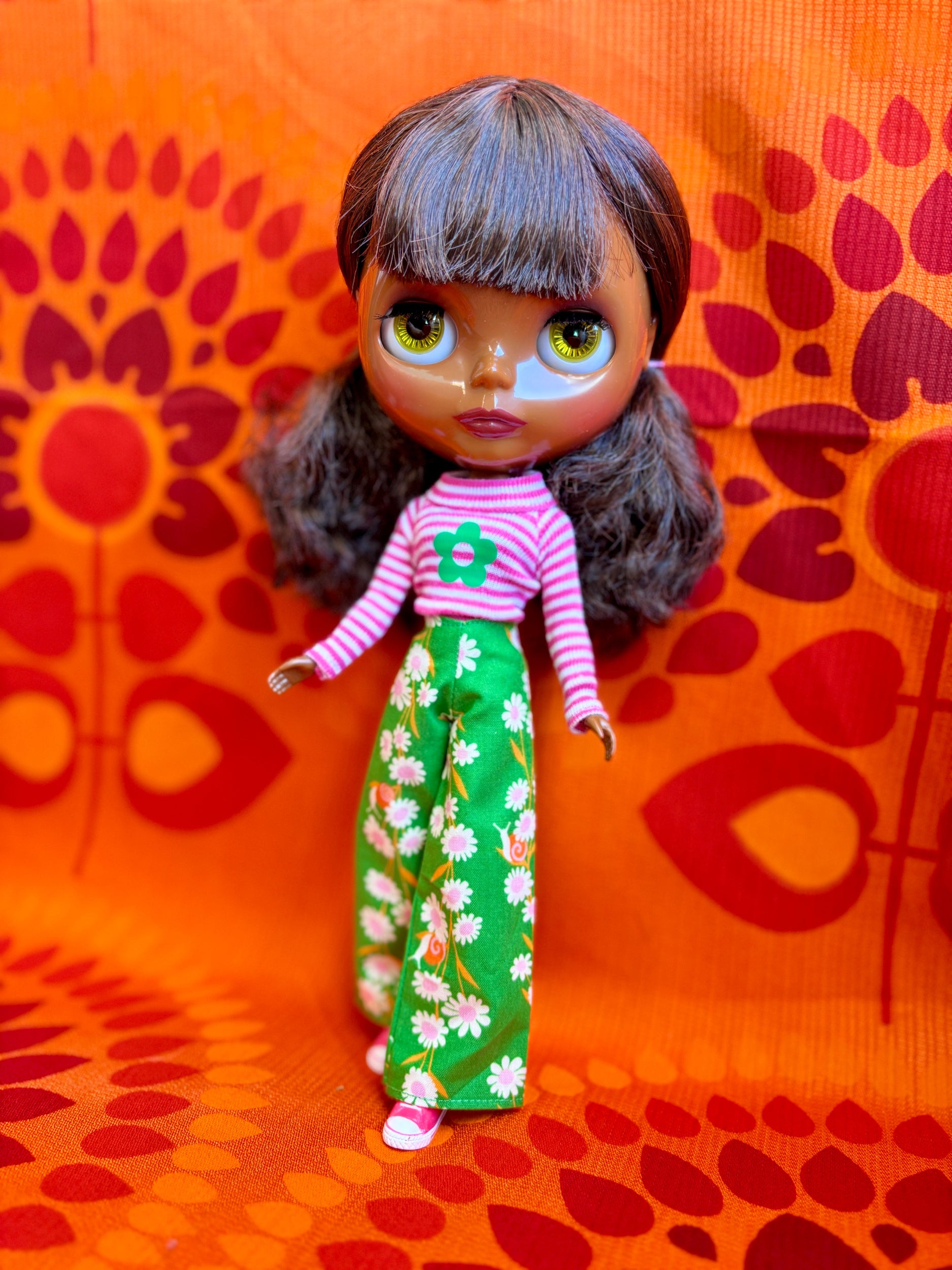 Doll with striped shirt and floral pants on a patterned orange background