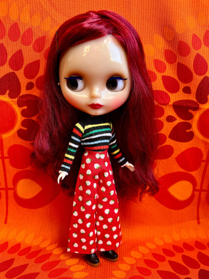 Doll with red hair wearing a striped shirt and red polka dot skirt against an orange background