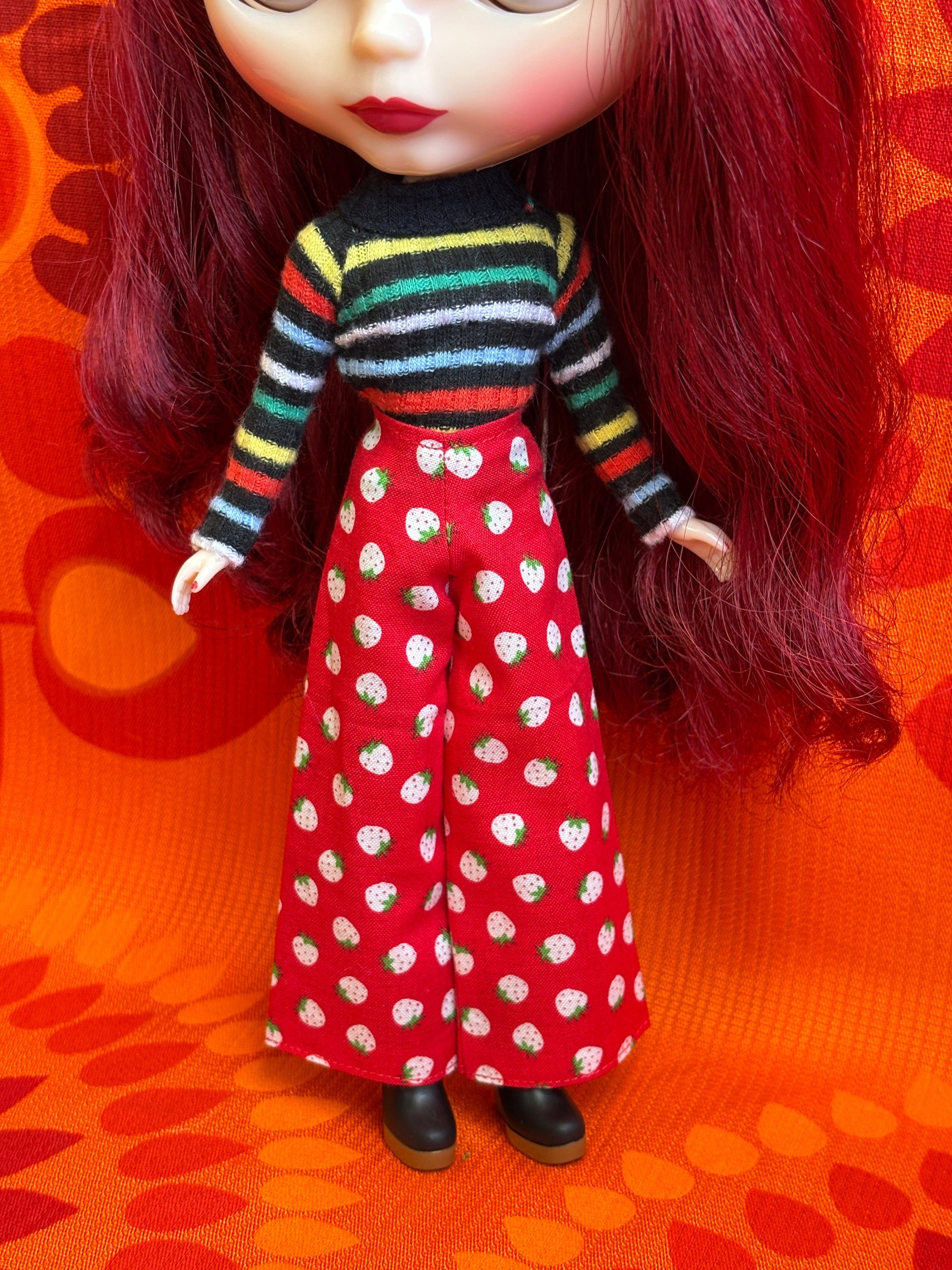 Doll with red hair and colorful outfit on an orange patterned background