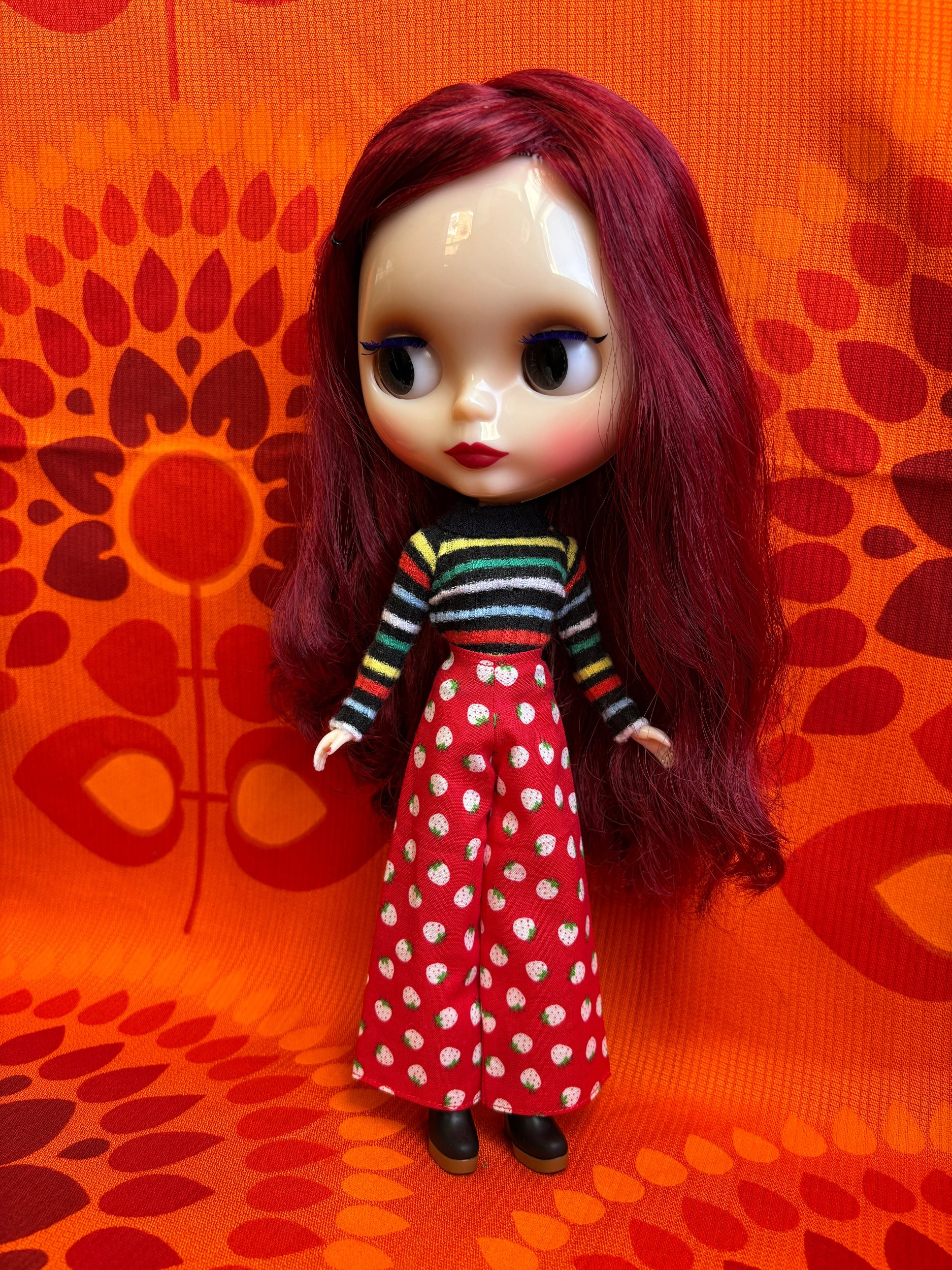 Doll with red hair and a striped outfit on an orange patterned surface