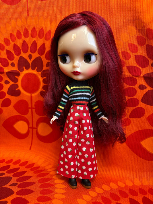 Doll with red hair and a striped outfit on an orange patterned surface