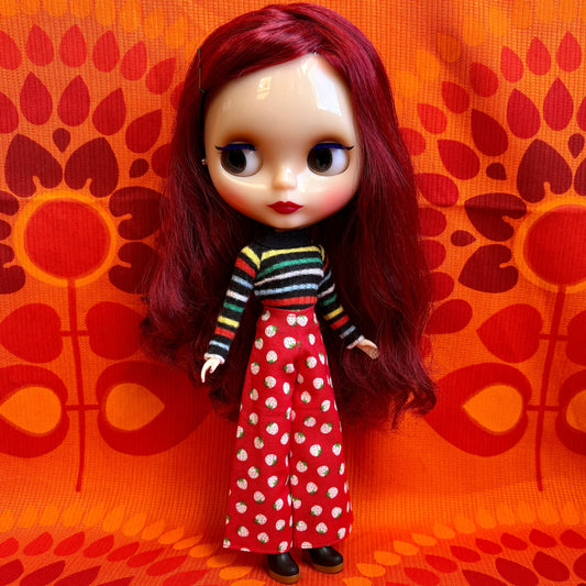 Doll with red hair wearing a striped shirt and polka dot pants against an orange patterned background