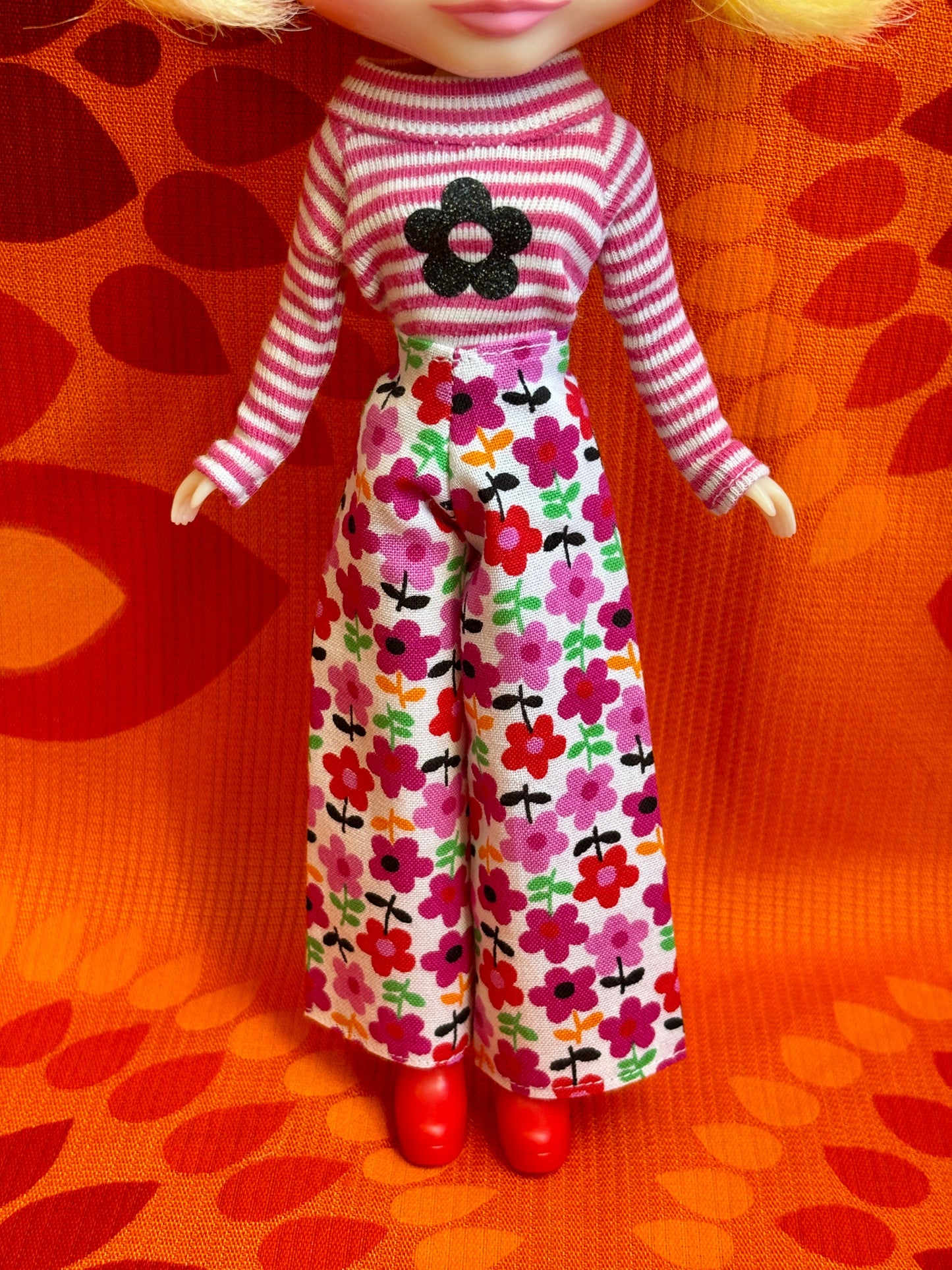 Doll wearing a striped sweater and floral pants on an orange patterned background