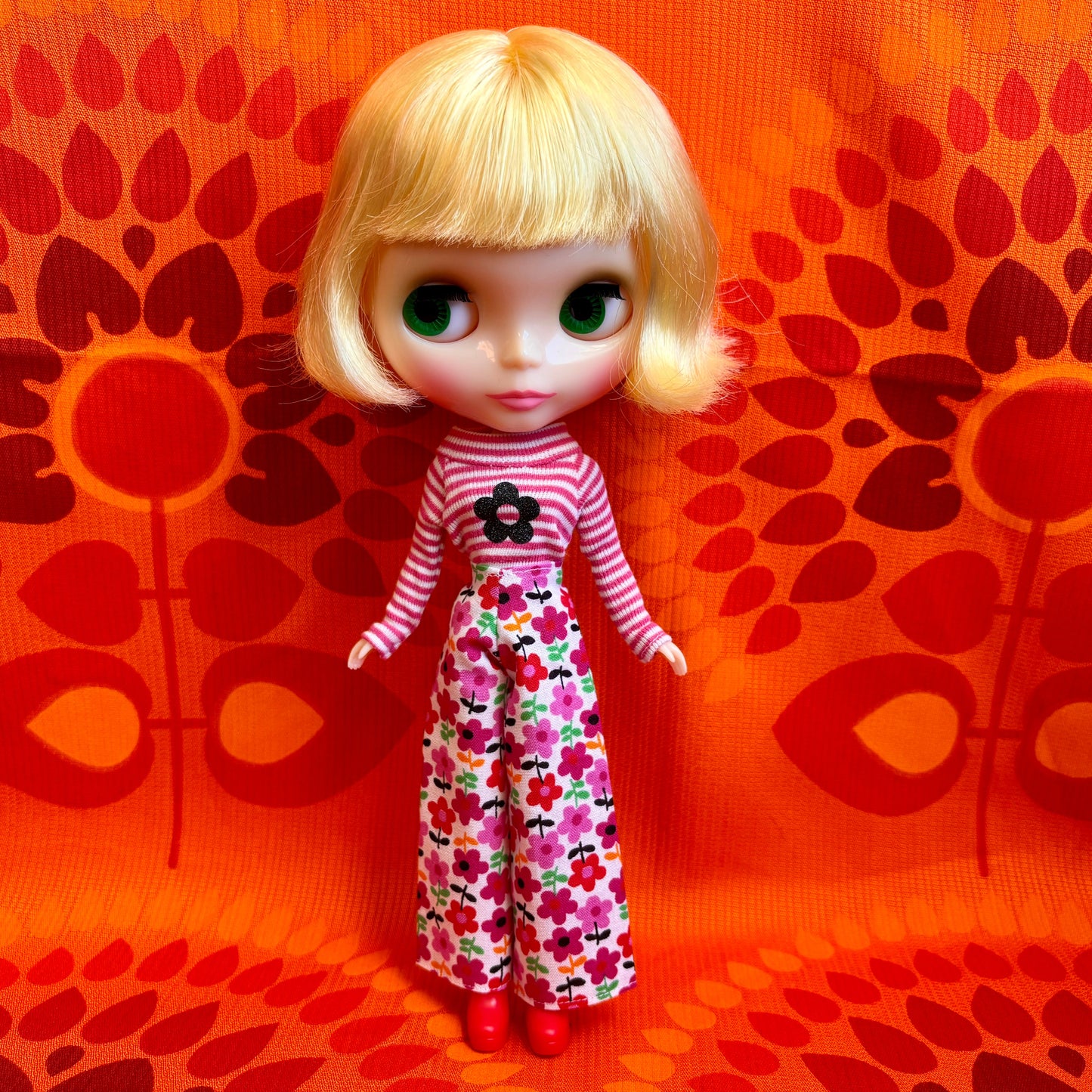 Doll with blonde hair and a striped outfit on an orange patterned background