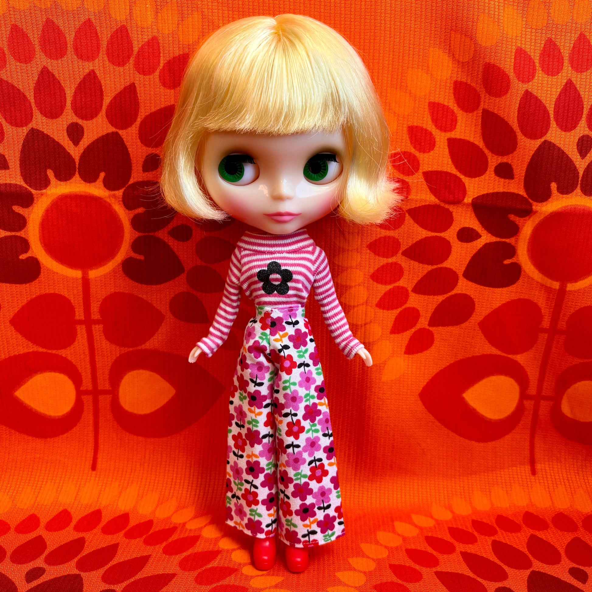 Doll with blonde hair and a striped outfit on an orange patterned background