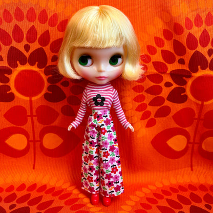 Doll with blonde hair and a striped outfit on an orange patterned background