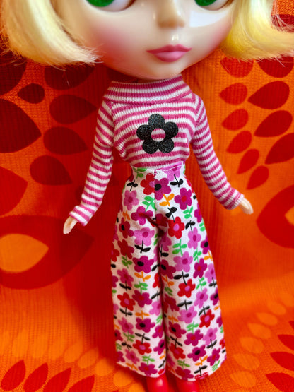 Doll wearing a striped shirt and floral pants on a patterned orange background