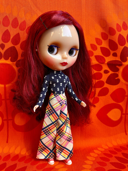 Doll with red hair and a patterned outfit on an orange background