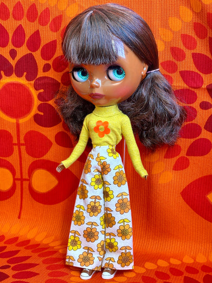 Doll wearing a yellow top and floral pants against an orange patterned background