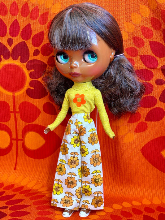 Doll wearing a yellow top and floral pants against an orange patterned background