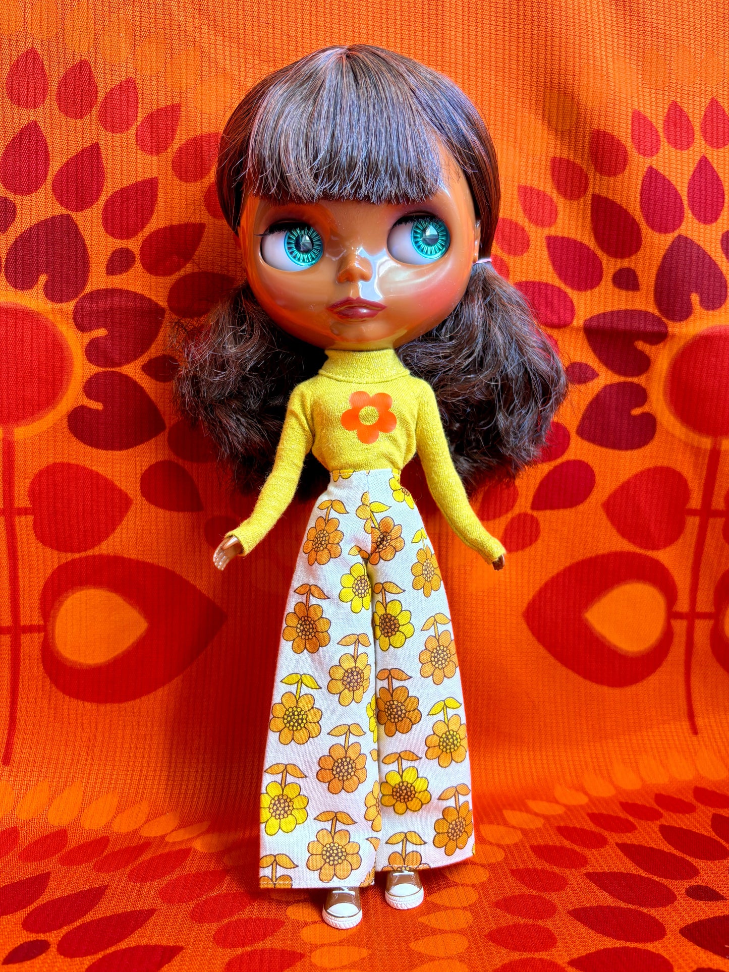 Doll with yellow top and floral pants on an orange patterned background