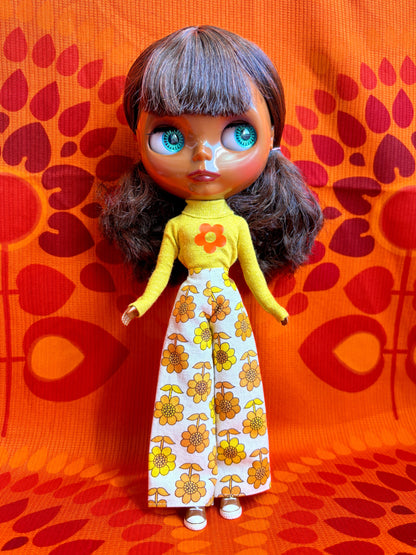 Doll with yellow top and floral pants on an orange patterned background
