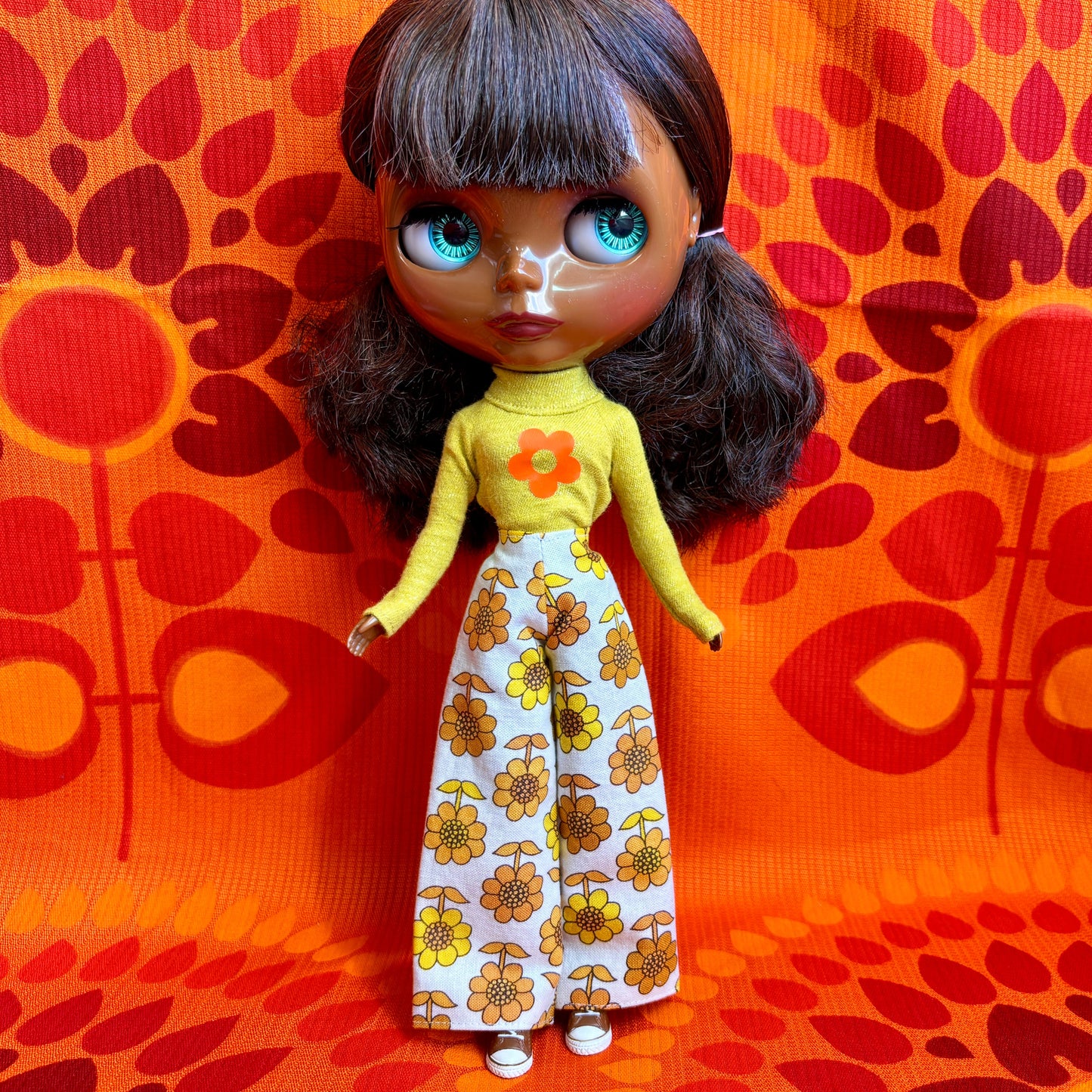 Doll with a yellow top and floral pants against an orange patterned background