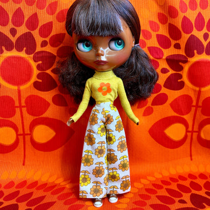 Doll with a yellow top and floral pants against an orange patterned background
