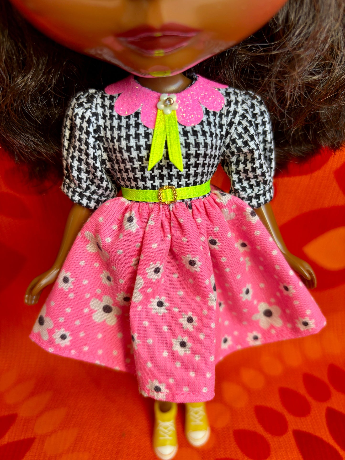 Doll wearing a black and white checkered top with a pink floral skirt on an orange background