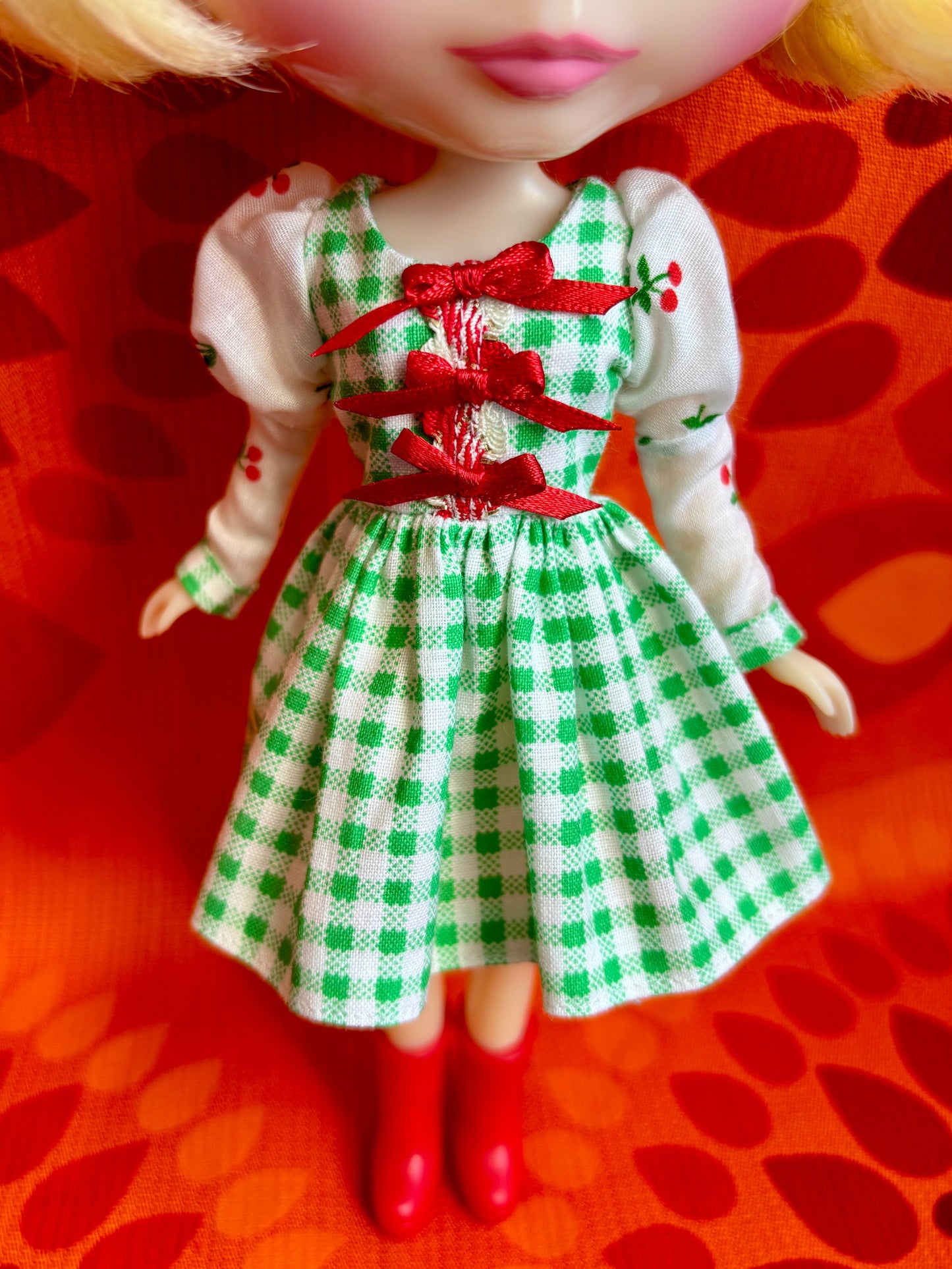 Doll wearing a green and white checkered dress with red accents on an orange background