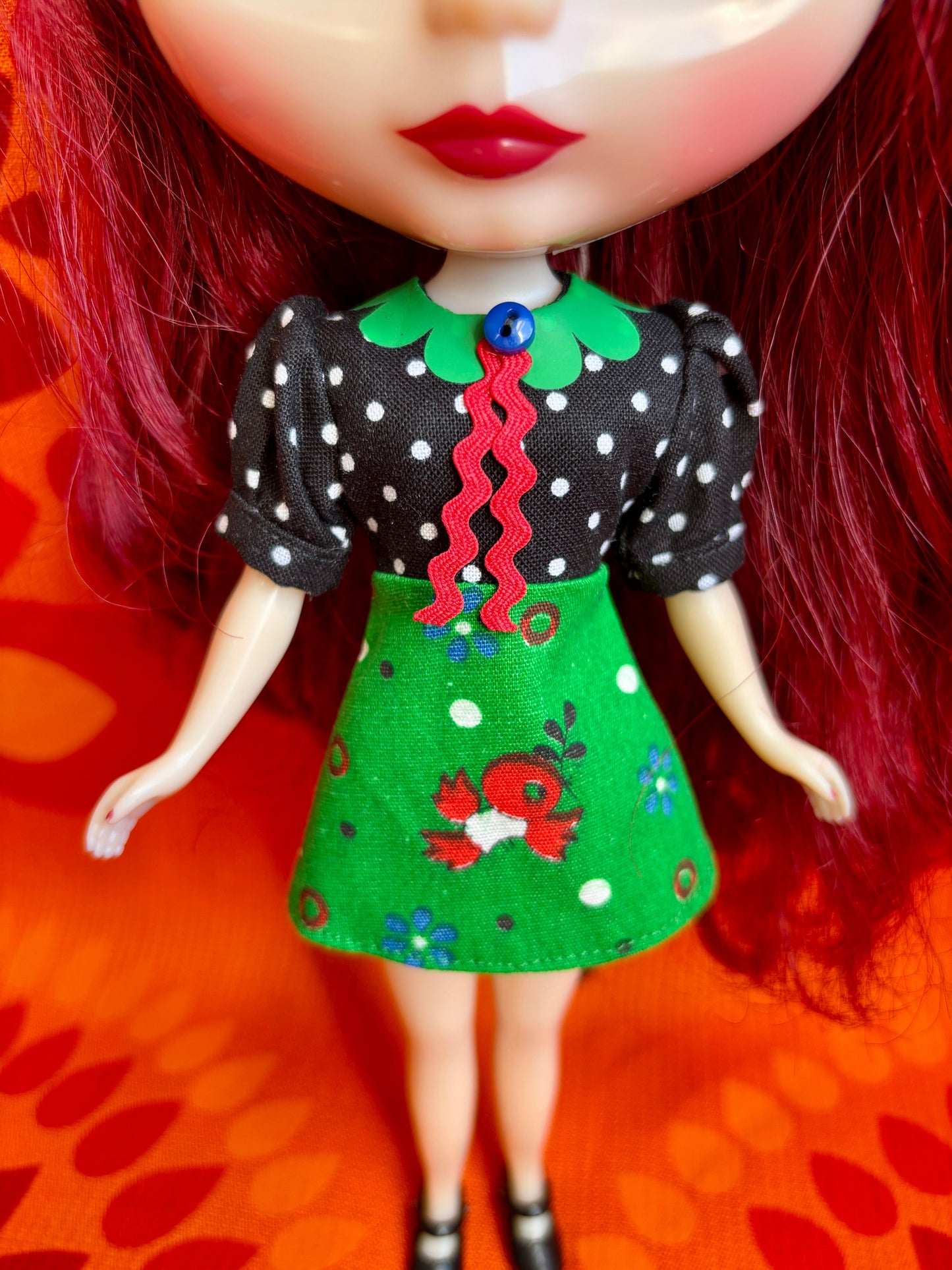 Doll with a black and white polka dot top and green skirt on an orange background