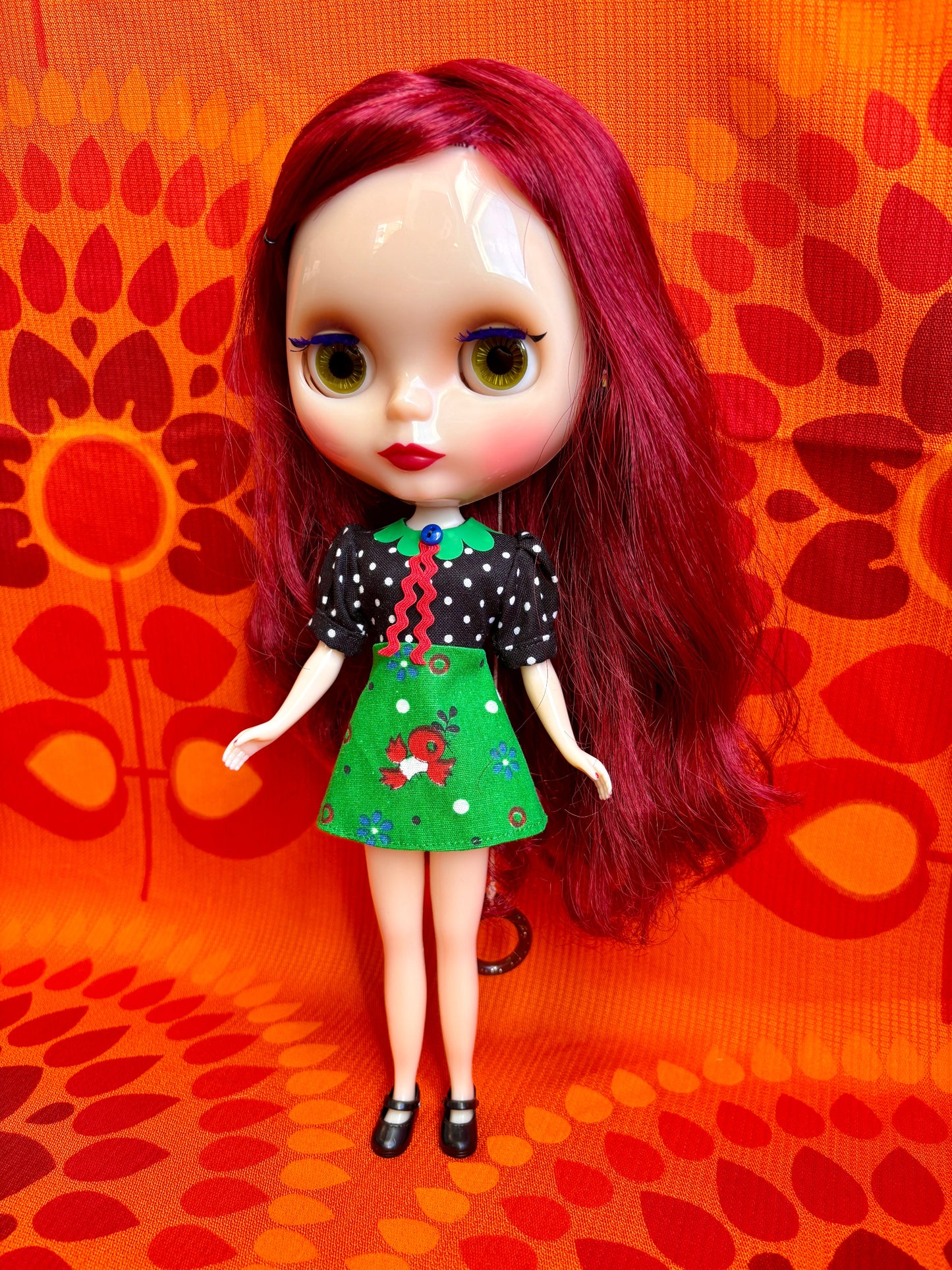 Doll with red hair and a black and green outfit on an orange patterned background