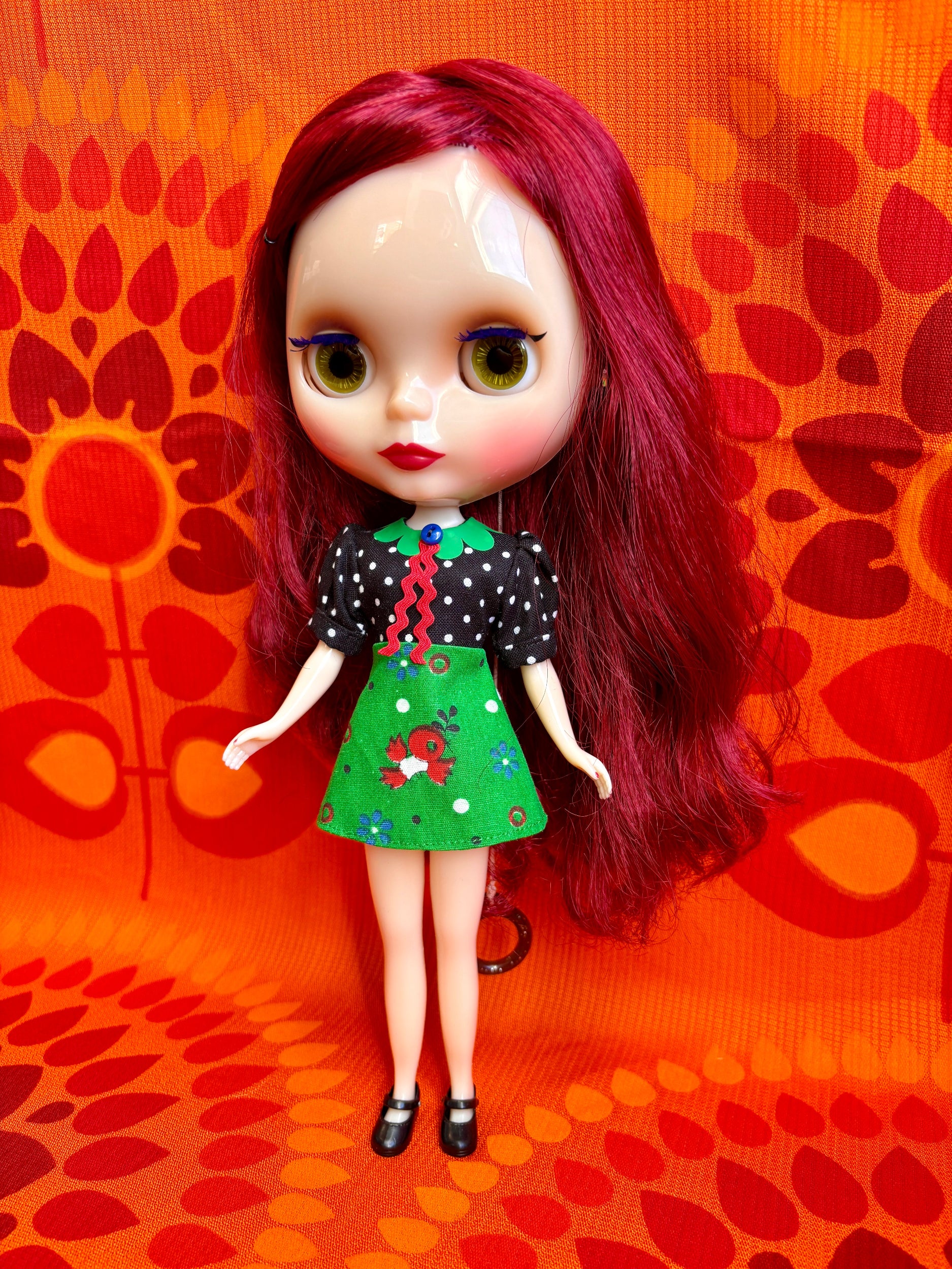 Doll with red hair and a black and green outfit on an orange patterned background
