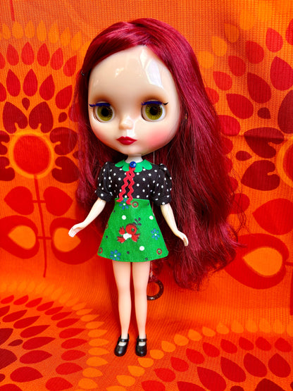 Doll with red hair and a black and green outfit on an orange patterned background