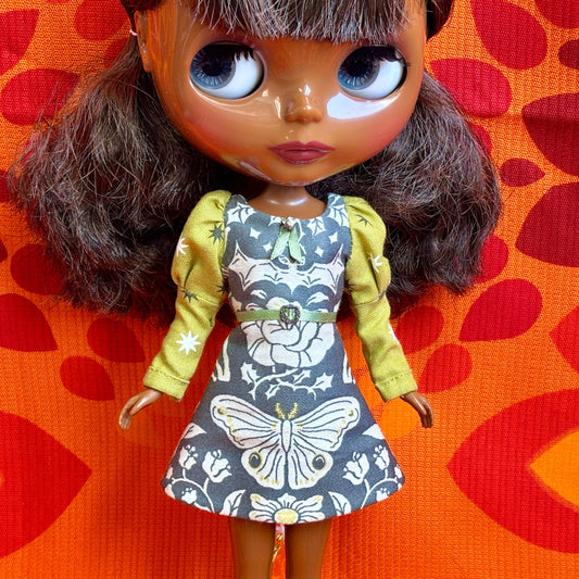 Doll wearing a patterned dress with a yellow cardigan on an orange background