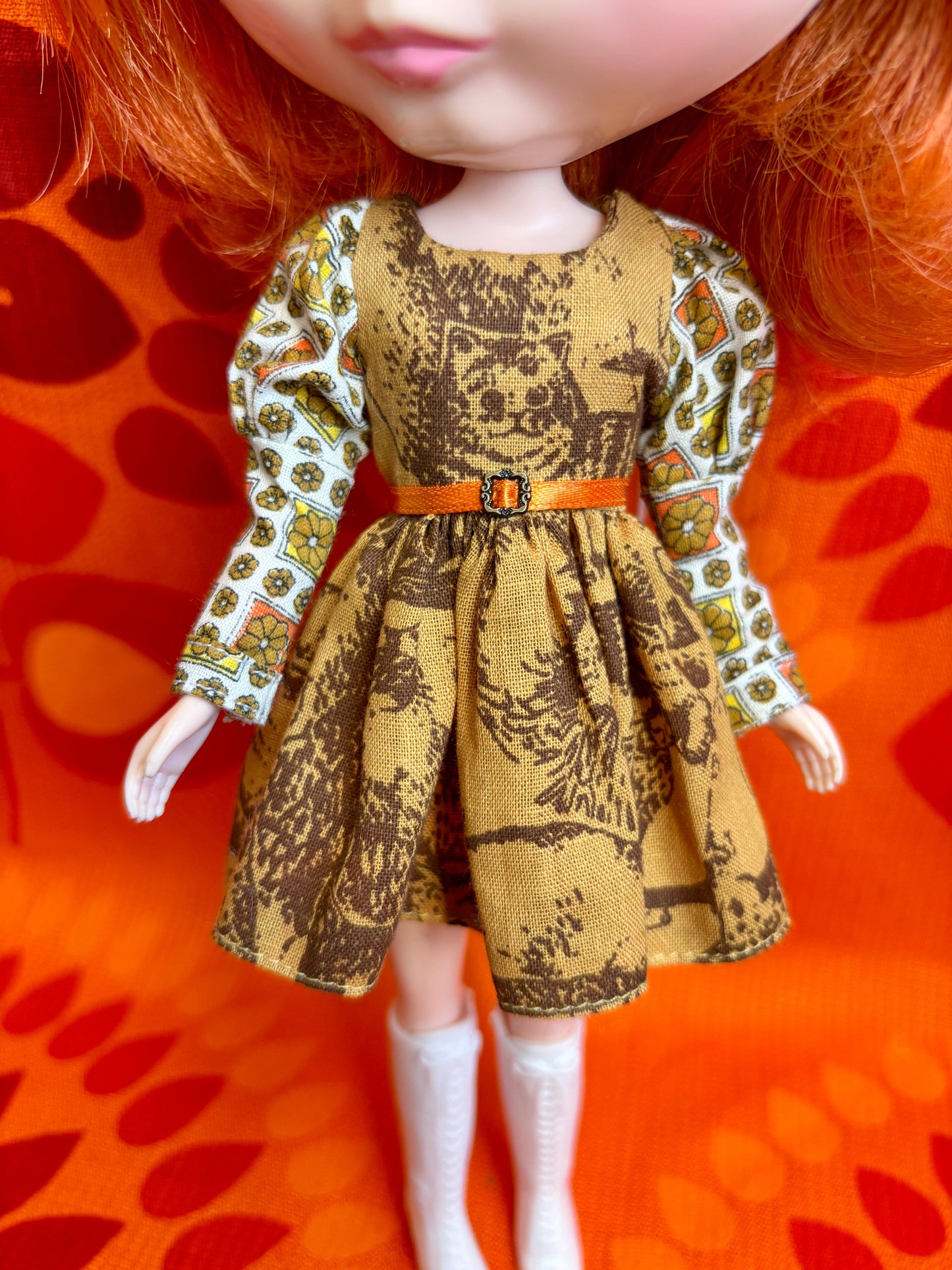 Doll wearing a patterned dress with a belt on an orange background