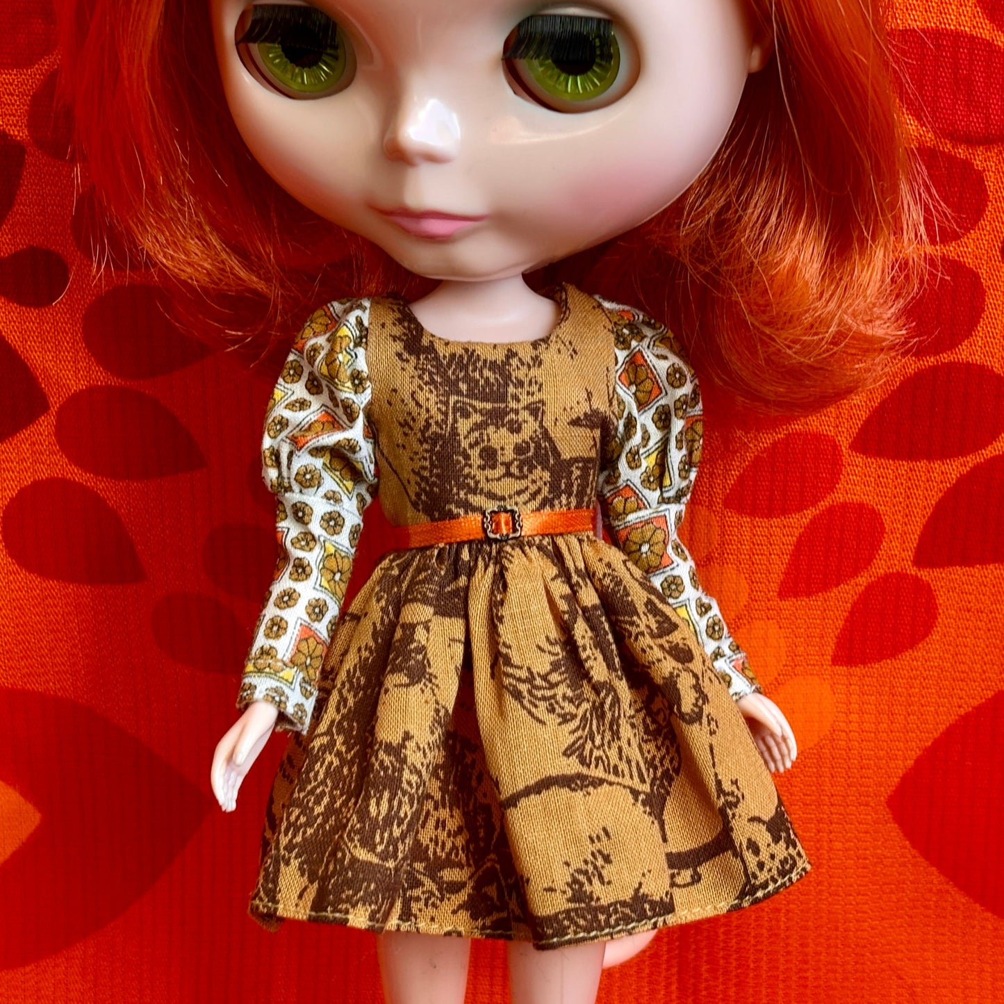 Doll wearing a patterned dress with a belt against an orange background