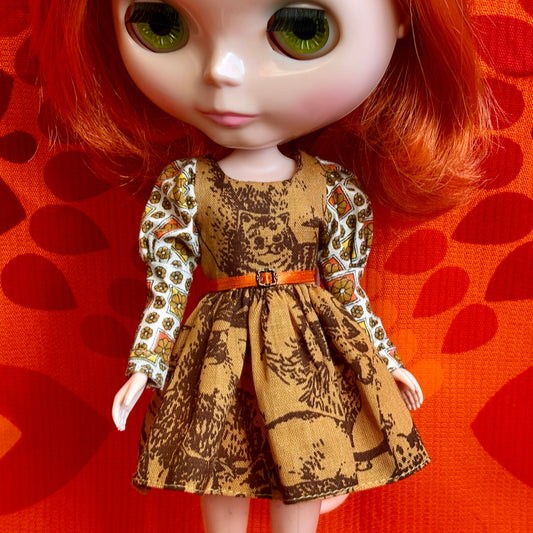 Doll wearing a patterned dress with a belt against an orange background