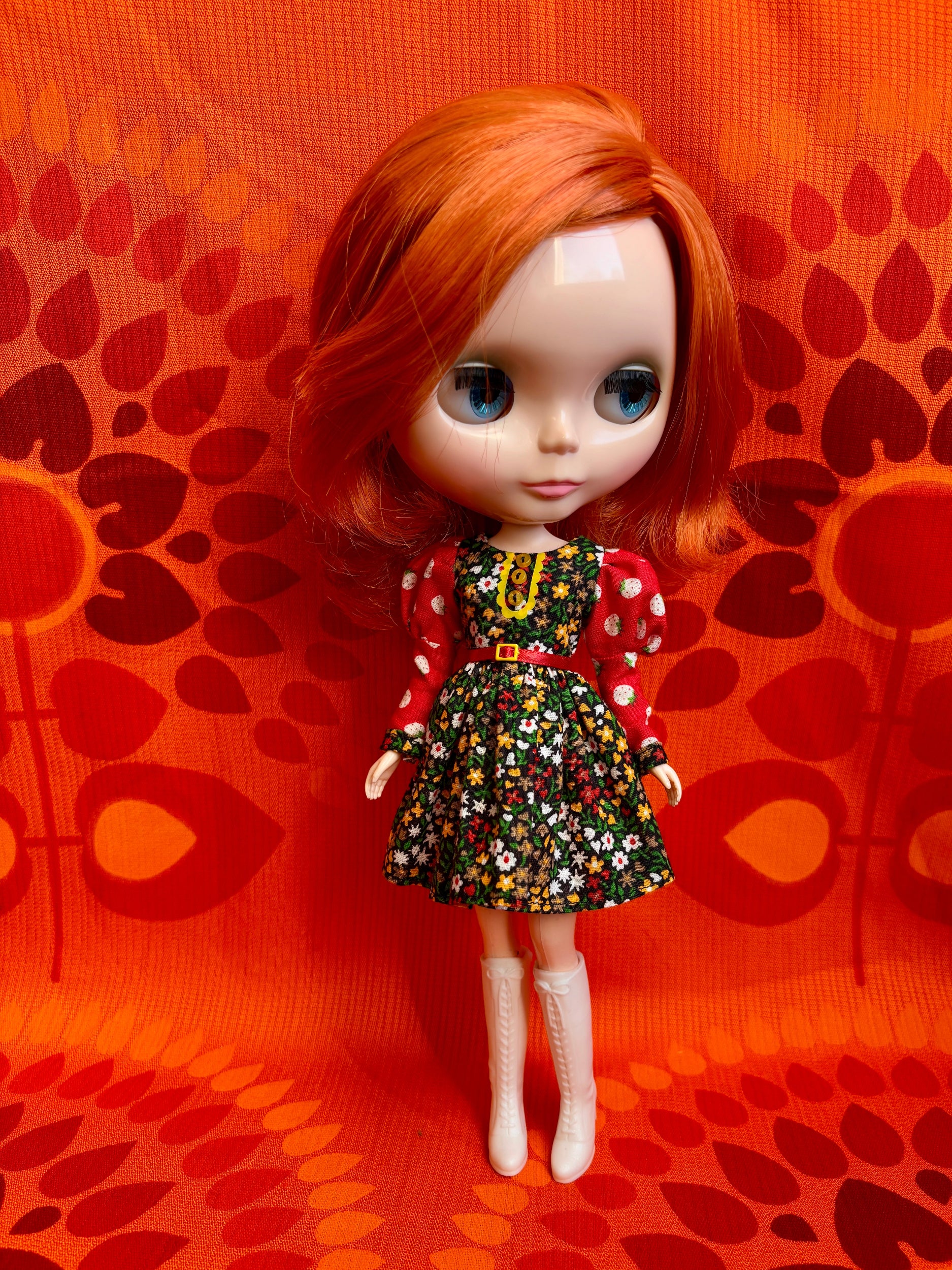Doll with red hair and a colorful dress on an orange patterned background