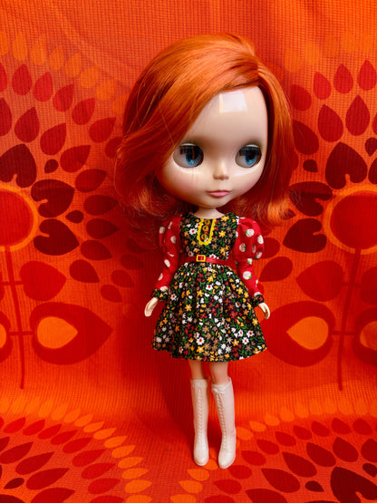 Doll with red hair and a colorful dress on an orange patterned background