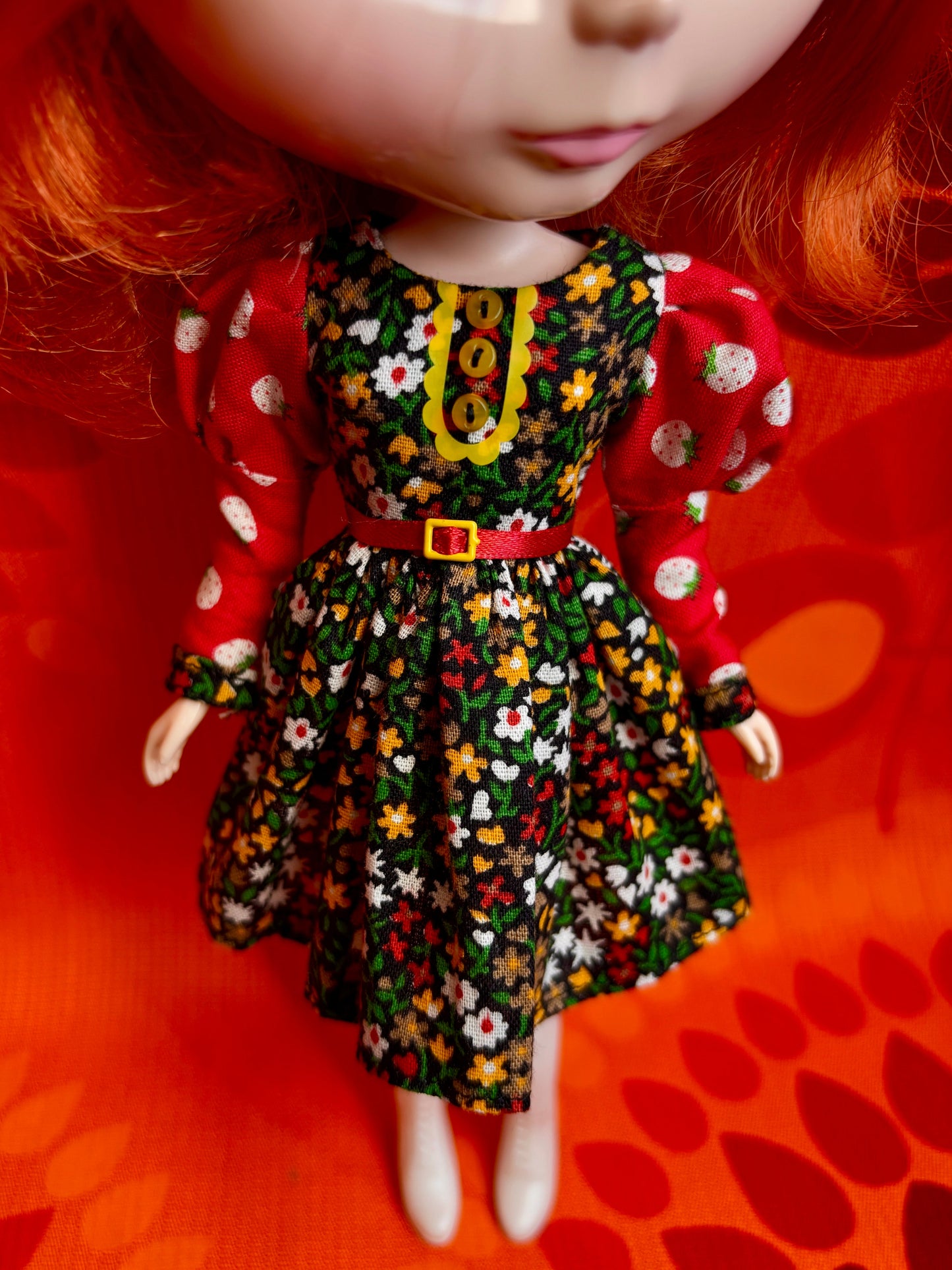 Doll wearing a floral dress with a red belt on an orange background