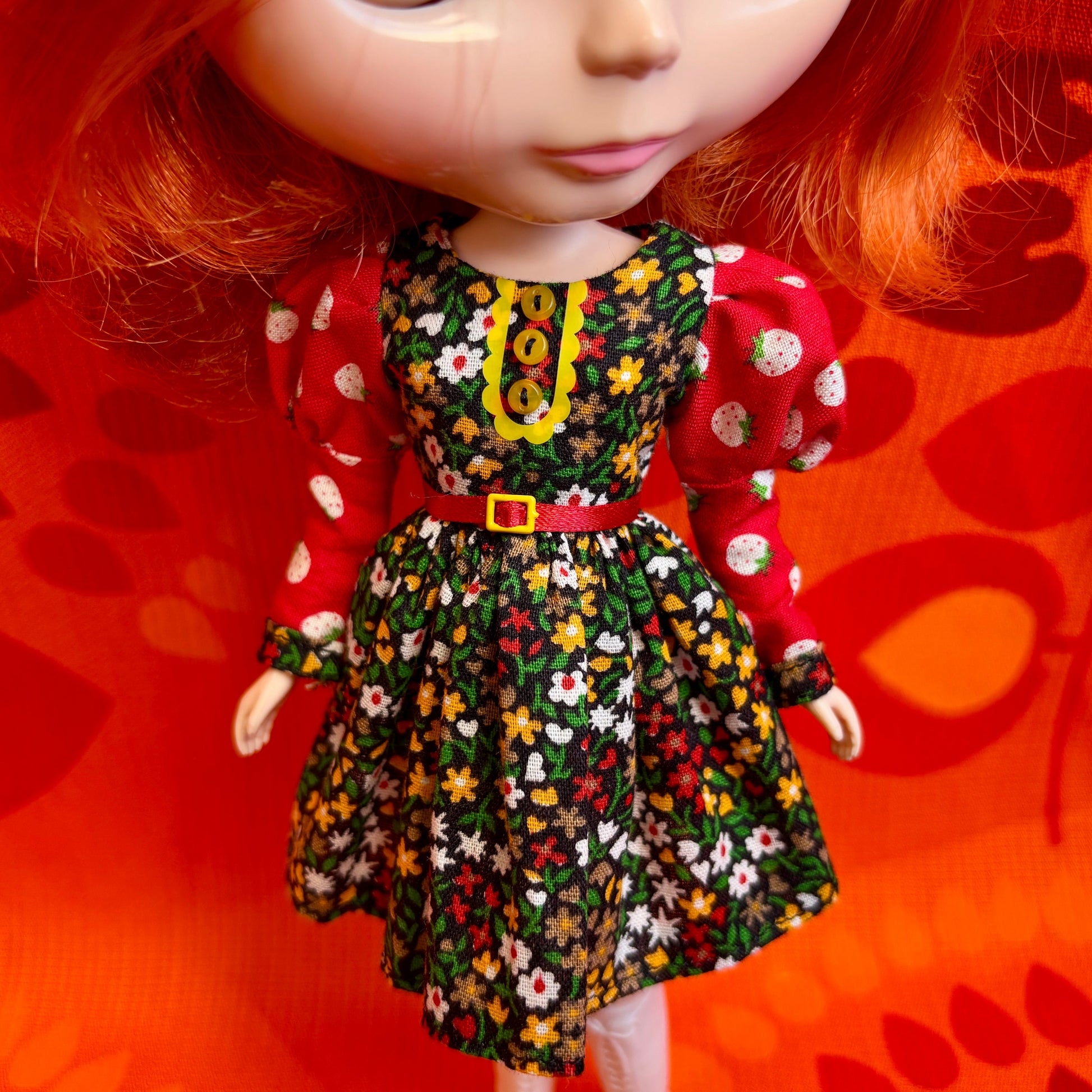Doll wearing a floral dress with a red belt against an orange background