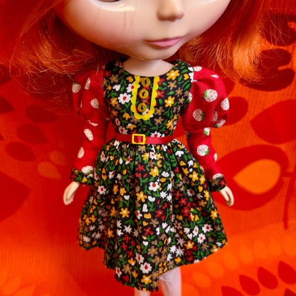 Doll wearing a floral dress with a red belt against an orange background