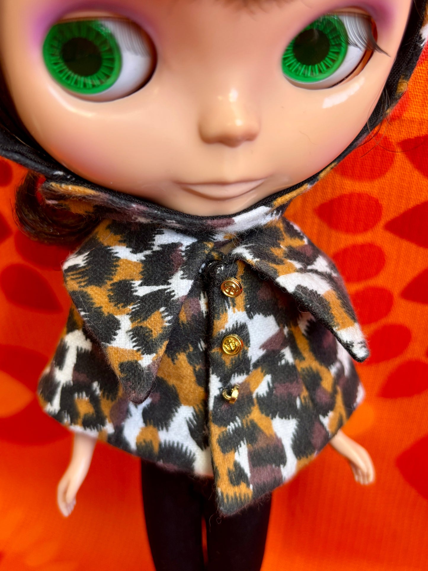 Close-up of a doll with a leopard print coat against an orange background