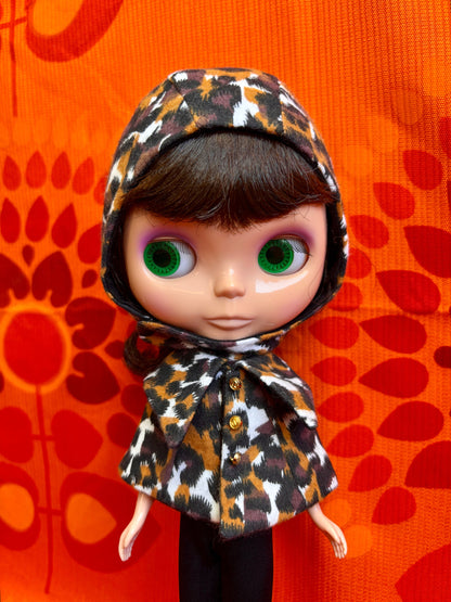 Doll wearing a leopard print outfit against an orange background with red abstract patterns