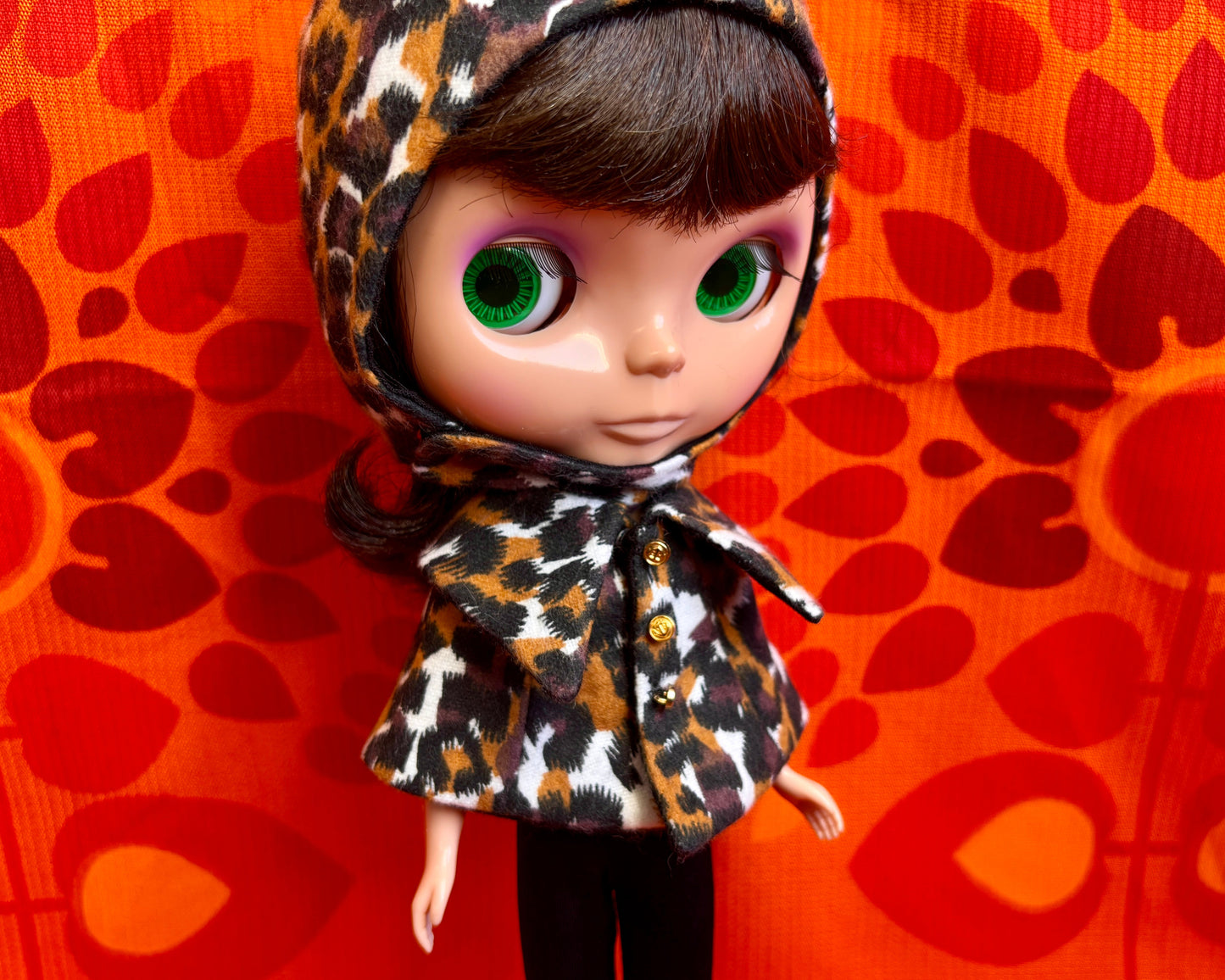 Doll wearing a leopard print hat against an orange patterned background