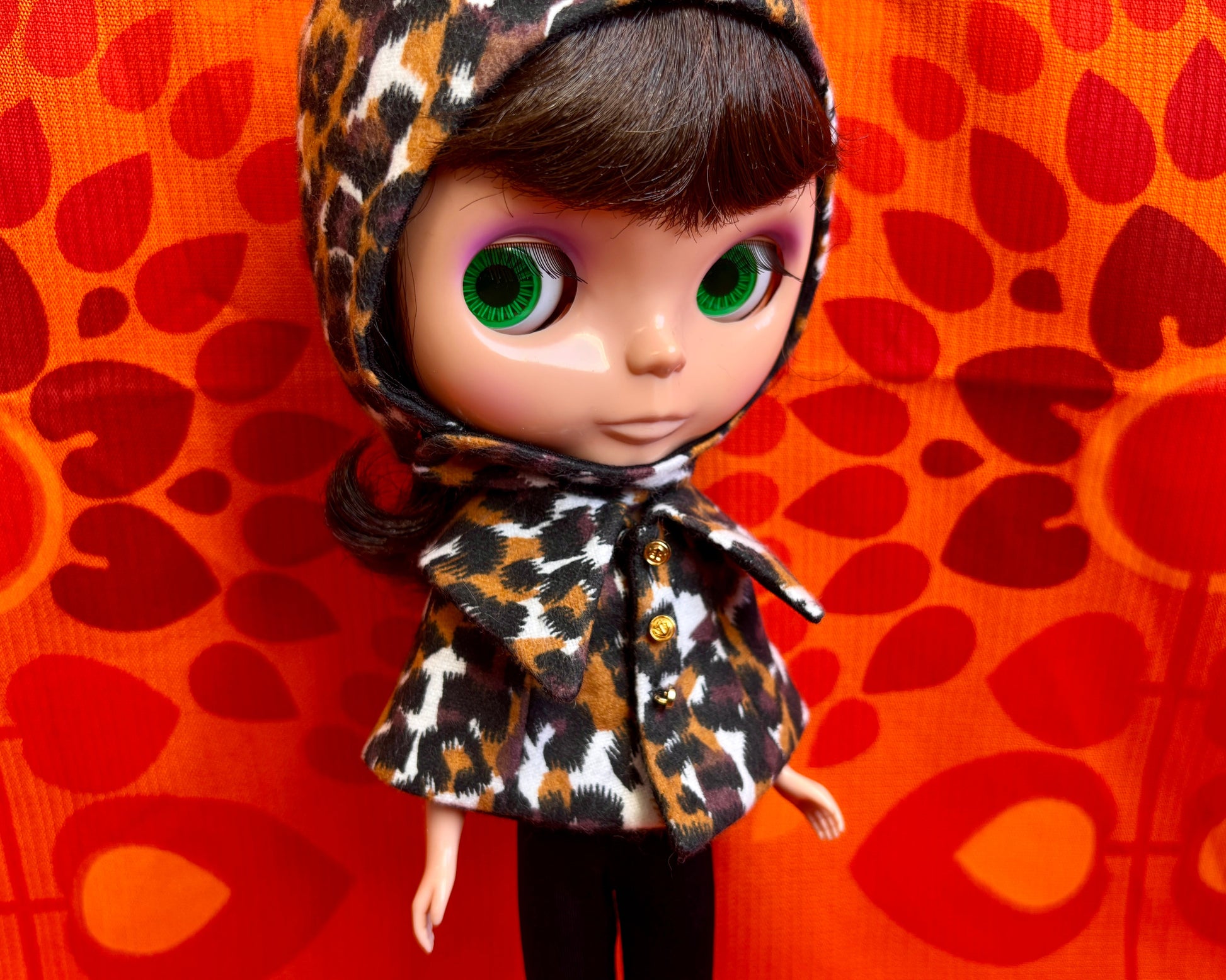 Doll wearing a leopard print hat against an orange patterned background