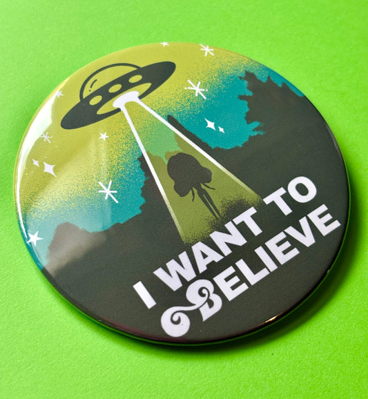 Button badge with UFO design and 'I Want to Believe' text on a green background